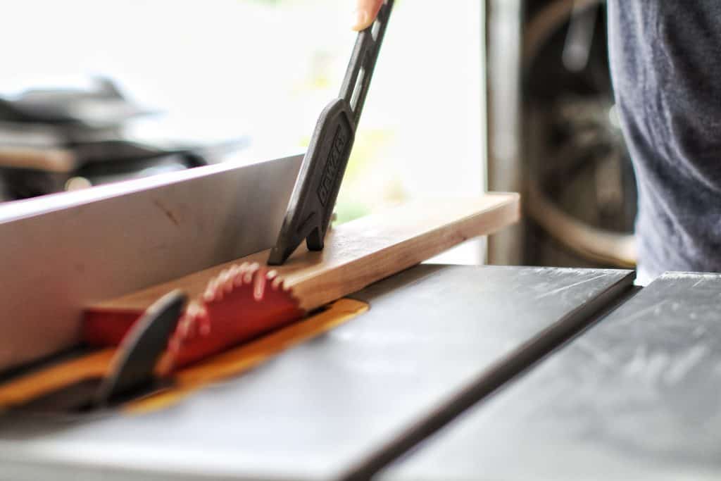 Man using a push stick to cut wood in a table saw
