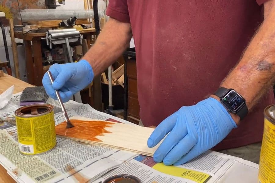 Man with gloved hands applying stain on a piece of wood