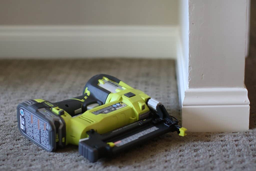 A green and black colored nailer near a white wall on a gray carpet