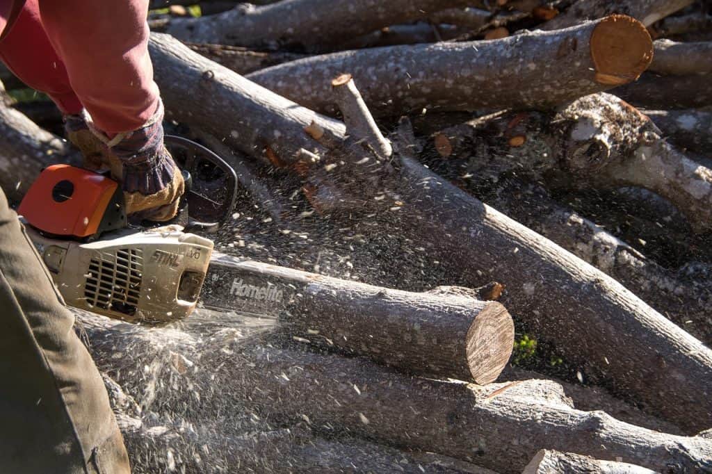 A person wearing protective gear cutting wood using a chainsaw