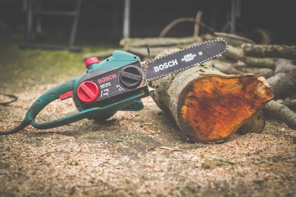 A green and black Bosch chainsaw with a black power cord is placed near a brown wooden log