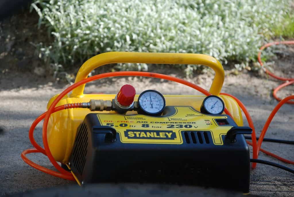A black and yellow Stanley air compressor with an orange hose near the green grass